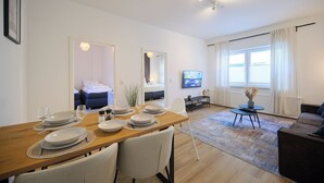 Een eetgedeelte met een houten tafel voor vier personen, een bank en een televisie op de achtergrond.