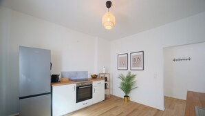 Een moderne keuken met een koelkast, oven en een houten aanrecht. Er hangen afbeeldingen in lijsten aan de muur en staat een plant in een pot.