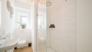 Een moderne badkamer met een douchecabine van glas, een wit wastafelmeubel en een toilet.
