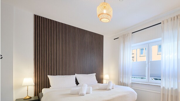 Hotelkamer met een groot bed, twee nachtkastjes, een hanglamp, een raam met gordijnen en uitzicht op gebouwen.