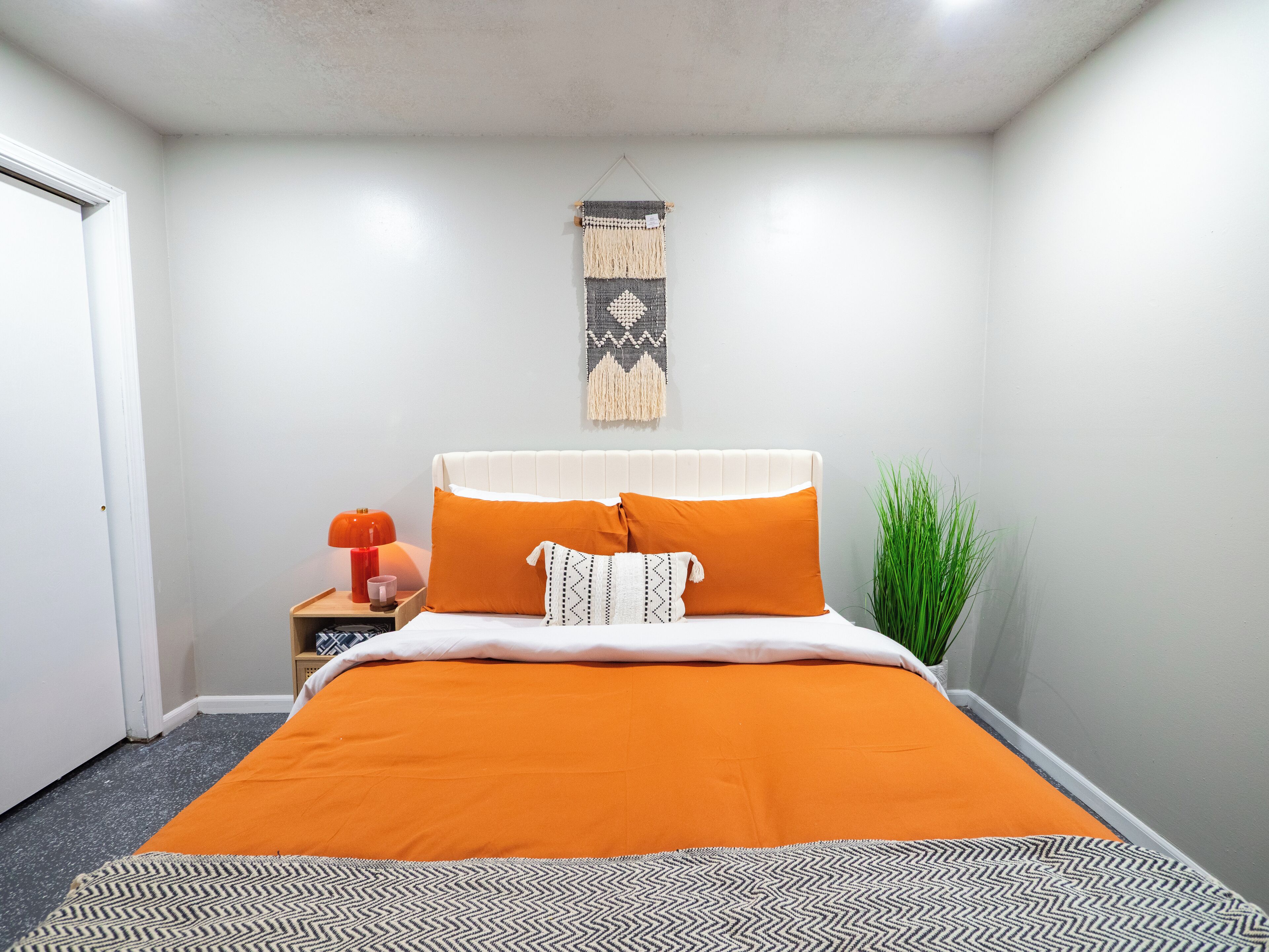 A bedroom with a bed, a nightstand, a lamp, and a wall hanging.