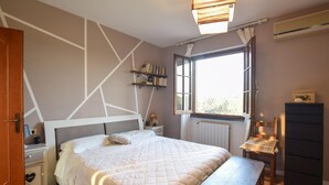 A bedroom with a bed, bedside tables, a nightstand, a window with curtains, a radiator, and a wooden bench. - Lovely home in Seravezza with WiFi (Seravezza)