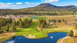 Un campo de golf con un estanque, rodeado de árboles y una montaña al fondo.
