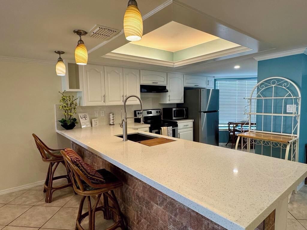 A kitchen with a large island, white cabinets, a stainless steel refrigerator, and a dining area with a metal chair and table.