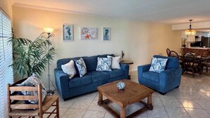 Una sala de estar con dos sofás azules, una mesa de centro de madera, una planta en maceta y un comedor con sillas y una mesa.
