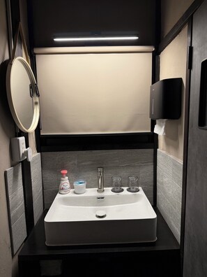 Een kleine badkamer met een witte wastafel, een spiegel, een handdroger en een fles handzeep.
