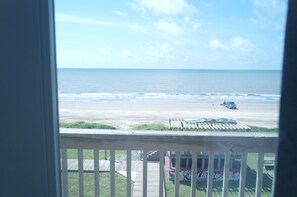 A view of the beach from a balcony with a wooden railing, a beach umbrella, and a beachside building with a mural.