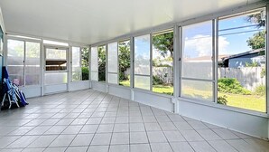 Habitación amplia con ventanas grandes, suelo de baldosas y vista a un patio trasero.