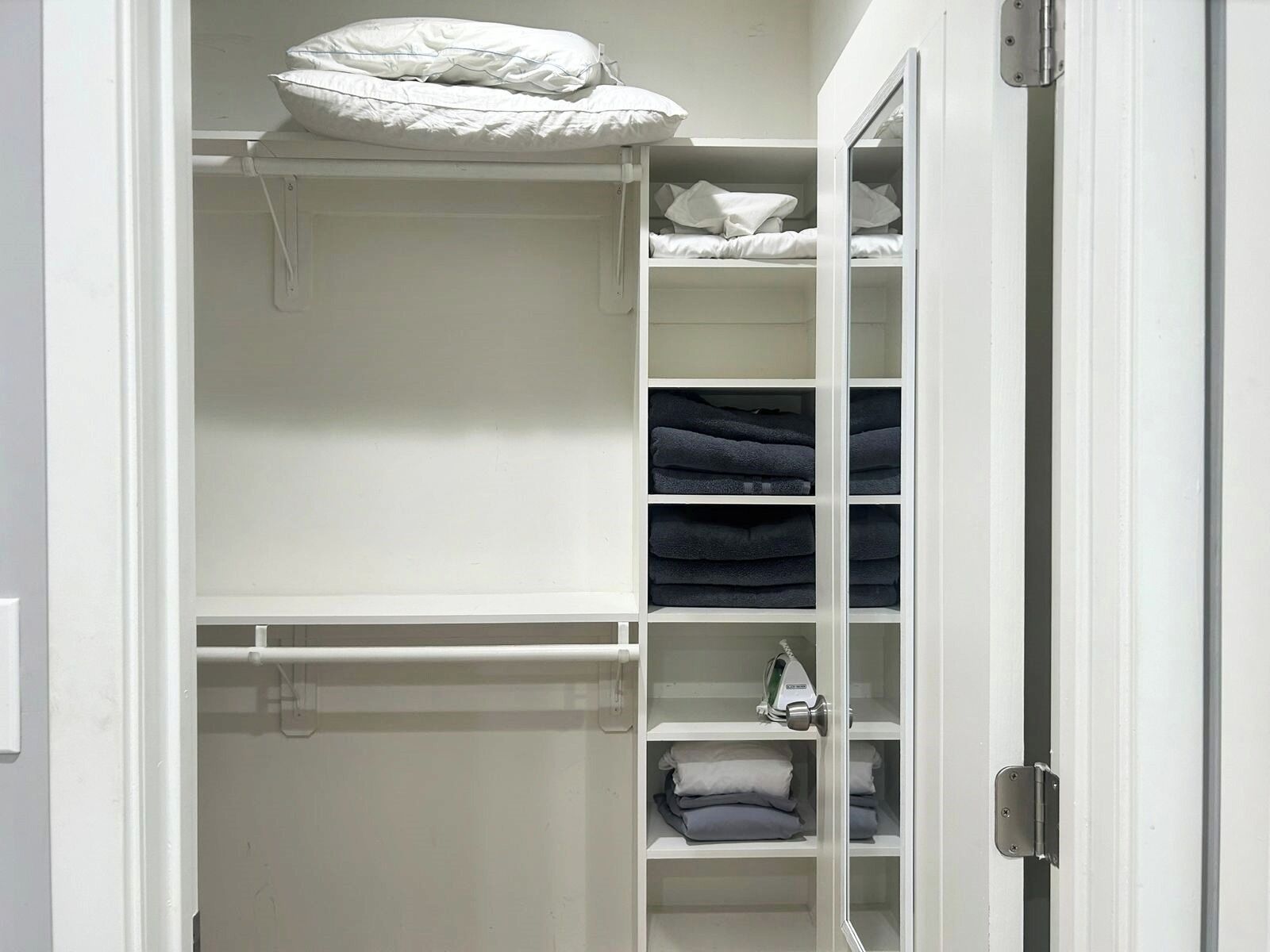 Un armario blanco con repisas para ropa doblada y espacio para colgar una almohada.