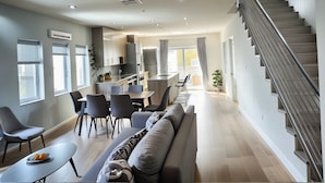 A modern kitchen with a dining area, a staircase, and a living room with a sofa and chairs.