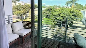 A balcony with a view of a cityscape, a wooden bench, and a cushioned chair.