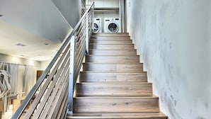 A modern staircase with wooden steps and metal railings, leading to a laundry area with two washing machines.