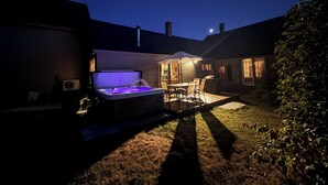 Un patio trasero con un jacuzzi, mobiliario de jardín y una zona de estar cubierta.