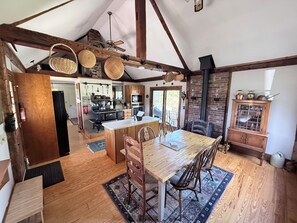 A rustic kitchen with wooden beams, a central island, and a dining area with chairs and a table.