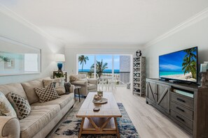 Salón con sofá, mesa de centro y televisión, con vistas a un balcón al mar.