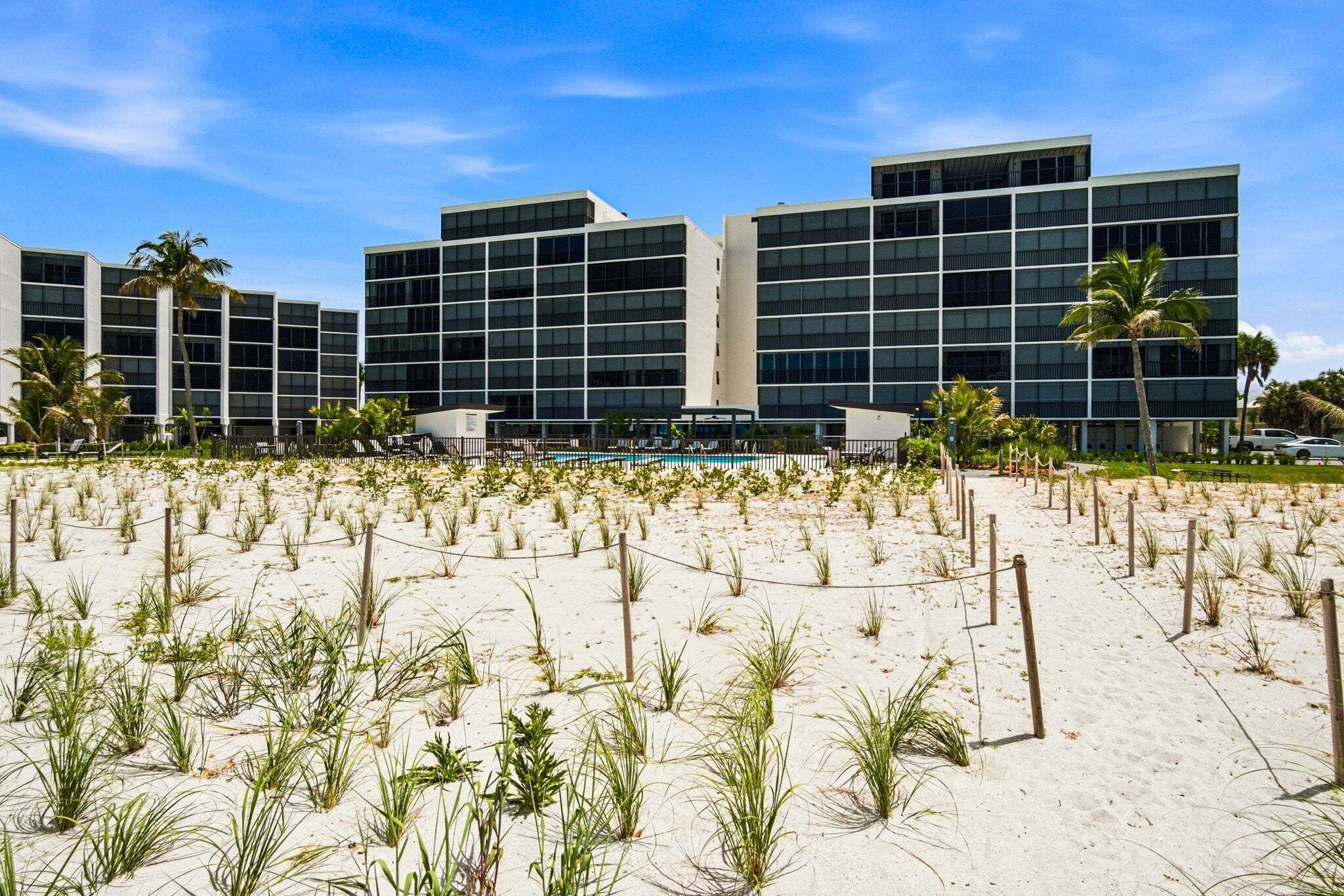 A modern hotel with multiple floors, a sandy beach in front, and palm trees.
