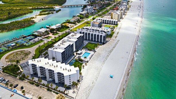 A coastal hotel with multiple buildings, a beach, and a marina. - Beachfront Condo | Pool, Pickleball, Tennis & More! (Bonita Springs)