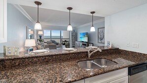 A kitchen with granite countertops, stainless steel sink, and pendant lighting. - Beachfront Condo | Pool, Pickleball, Tennis & More! (Bonita Springs)
