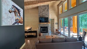 Una sala de estar moderna con chimenea de piedra, vigas de madera en el techo y grandes ventanales con vistas al exterior.