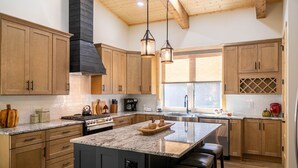 Una cocina amplia con armarios de madera, una isla grande con asientos, una estufa y un ventanal que proporciona luz natural.