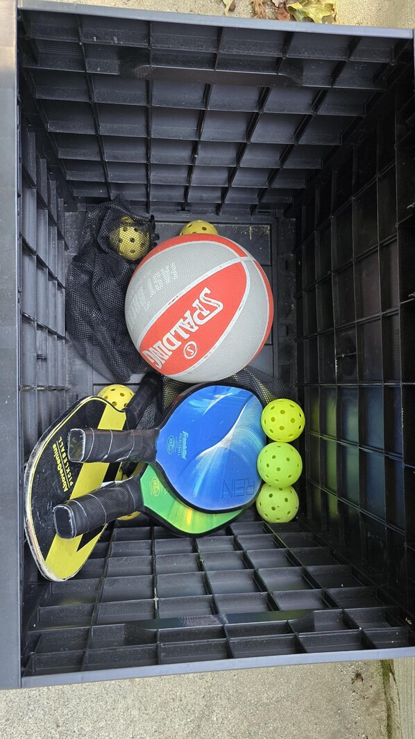 Un módulo de almacenamiento con suelo de rejilla negra, que contiene varios equipos deportivos, incluyendo una pala, una pelota de tenis y un casco amarillo.