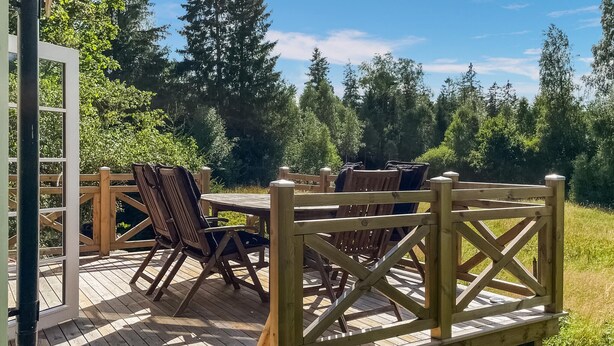 A wooden deck with a table and chairs, surrounded by a wooden fence and lush greenery.