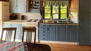A kitchen with a stove, sink, and cabinets. There is a window with a checkered valance and a view of greenery outside.