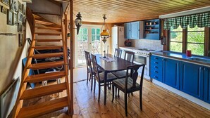 A wooden staircase leading to a dining area with a table and chairs, a kitchen with blue cabinets, and a view of greenery outside.