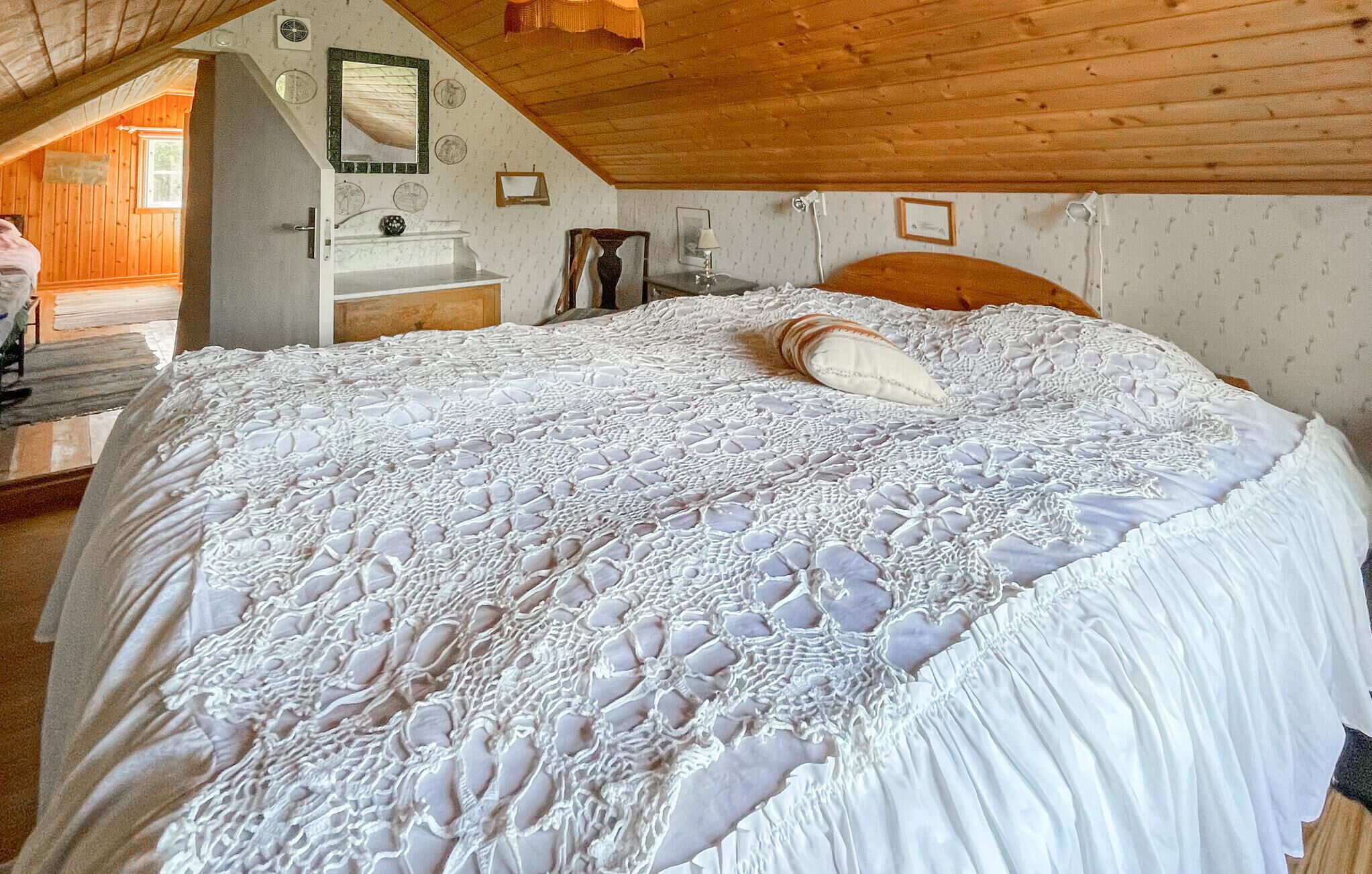 Een slaapkamer met een groot bed, een houten plafond en uitzicht op een houten hutje door een open deur.