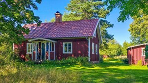A red wooden house with a tiled roof, surrounded by lush greenery and trees.