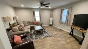 A living room with a sectional sofa, a coffee table, a TV on a stand, and a ceiling fan. - 3 Br Gem in Downtown Mooresville (Mooresville)