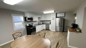 A modern kitchen with white cabinets, stainless steel appliances, and a wooden dining table. - 3 Br Gem in Downtown Mooresville (Mooresville)
