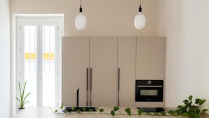 Eine moderne Küche mit einer großen Kochinsel, zwei Pendelleuchten, einem eingebauten Backofen und einer Tür mit Blick ins Freie.