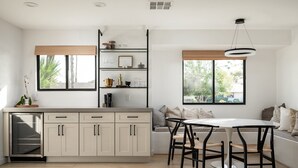 A modern kitchen with a built-in dishwasher, a dining area with a round table and chairs, and a large window with a view of greenery.