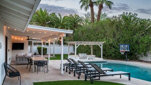 A backyard with a pool, outdoor seating, a barbecue area, and a basketball hoop.