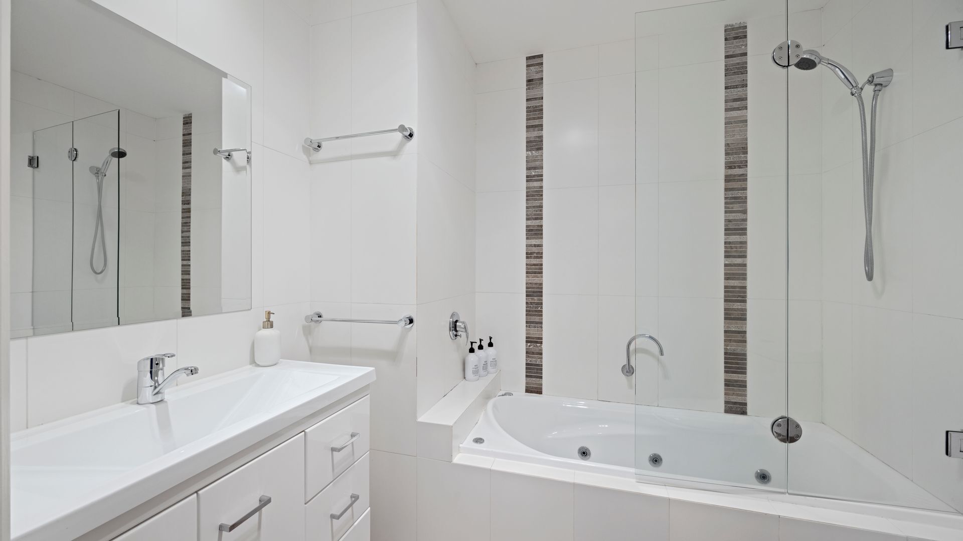 A modern bathroom with a large mirror, a white sink, a bathtub, and a shower area.