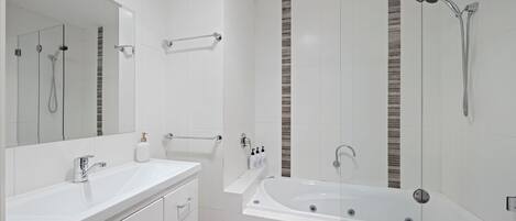 A modern bathroom with a large mirror, a white sink, a bathtub, and a shower area.