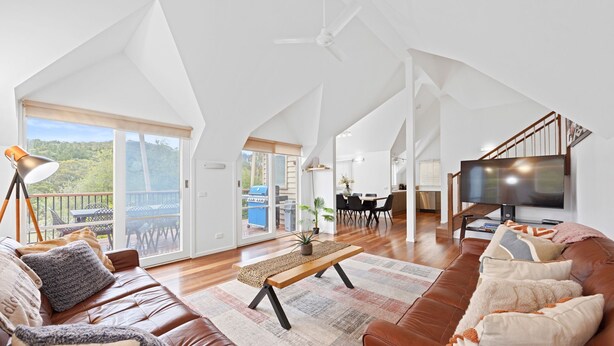 Un loft espacioso con techo alto, televisor grande y balcón con vistas al exterior.