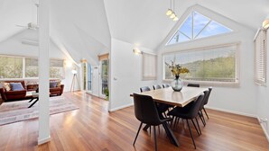 Una habitación amplia con techo alto, una mesa de comedor con sillas, un sofá y un gran ventanal con persianas.