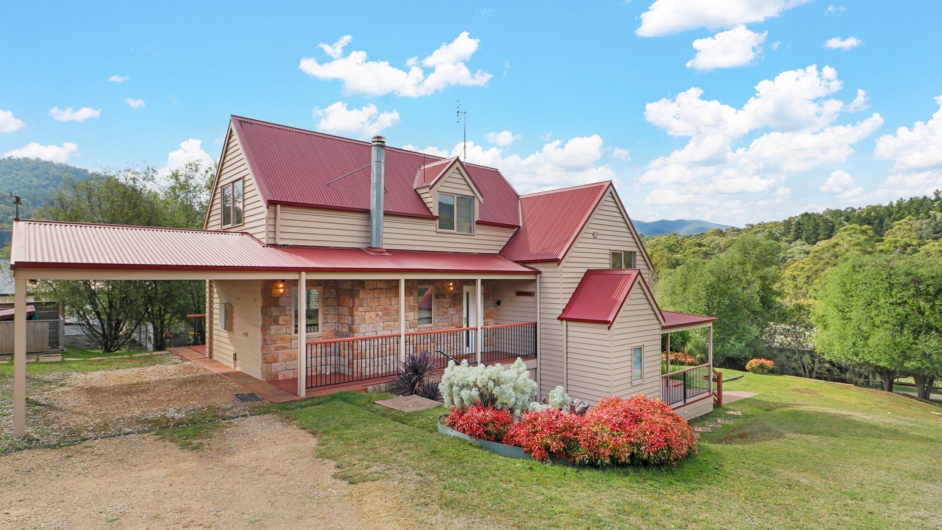 A two-story house with a red roof, stone foundation, and a covered porch.