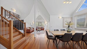 Amplia sala de estar con una escalera de madera, una mesa de comedor con sillas y una zona de estar acogedora con un sofá.
