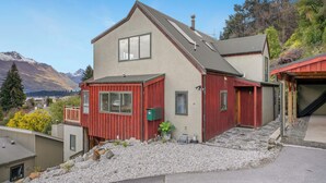 A two-story house with a red exterior, a grey roof, and a view of mountains in the background.