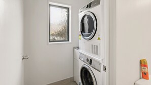 A laundry room with a front-loading washer and dryer, a window, and a door.