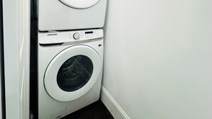 Una lavadora y secadora apiladas en una esquina de una habitación con suelo de madera oscura.