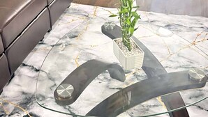 Una sala de estar con una mesa de centro de vidrio con diseño de mármol, un sofá de cuero marrón y una planta en maceta sobre la mesa.