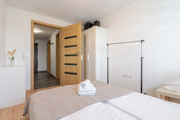 Ein Hotelzimmer mit Bett, Schrank, Spiegel, einem kleinen Tisch mit Vase und einer Tür zu einem weiteren Raum.