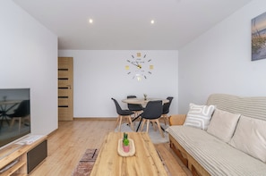 Ein modernes Wohnzimmer mit Essbereich, einem Holztisch, einer Couch und einer Wanduhr.