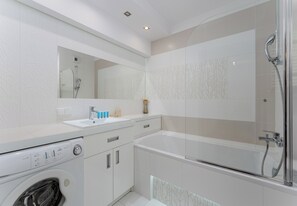 Un bany modern amb rentadora, un lavabo i zona de dutxa amb envidriament.