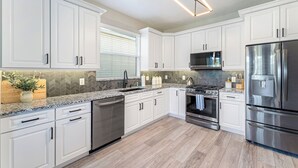 A modern kitchen with white cabinets, stainless steel appliances, and a herringbone tile backsplash.