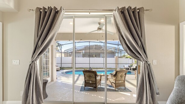 A room with a sliding glass door leading to an outdoor area with a pool and wicker furniture.